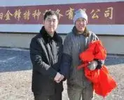 Two men holding a red ribbon outside the factory